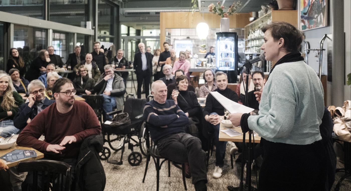 Een groep mensen in een zaal bij de lancering van het Vrienden van de Boon-fonds, één spreker en groepen mensen aan tafeltjes