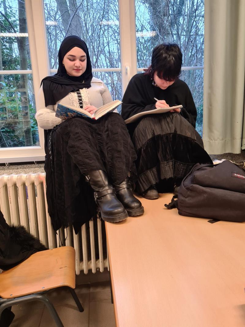 Twee leerlingen zitten op de vensterbank te lezen met hun voeten op tafel