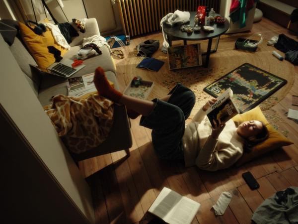 Een meisje ligt op de grond te lezen in een rommelige kamer