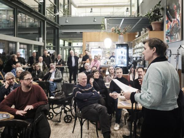Een groep mensen in een zaal bij de lancering van het Vrienden van de Boon-fonds, één spreker en groepen mensen aan tafeltjes